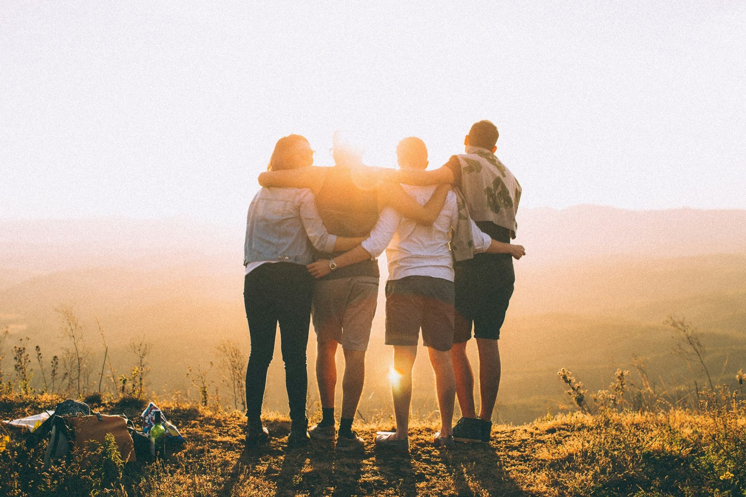 Four friends standing arm-in-arm on a hill at sunset, enjoying nature and each other's company.